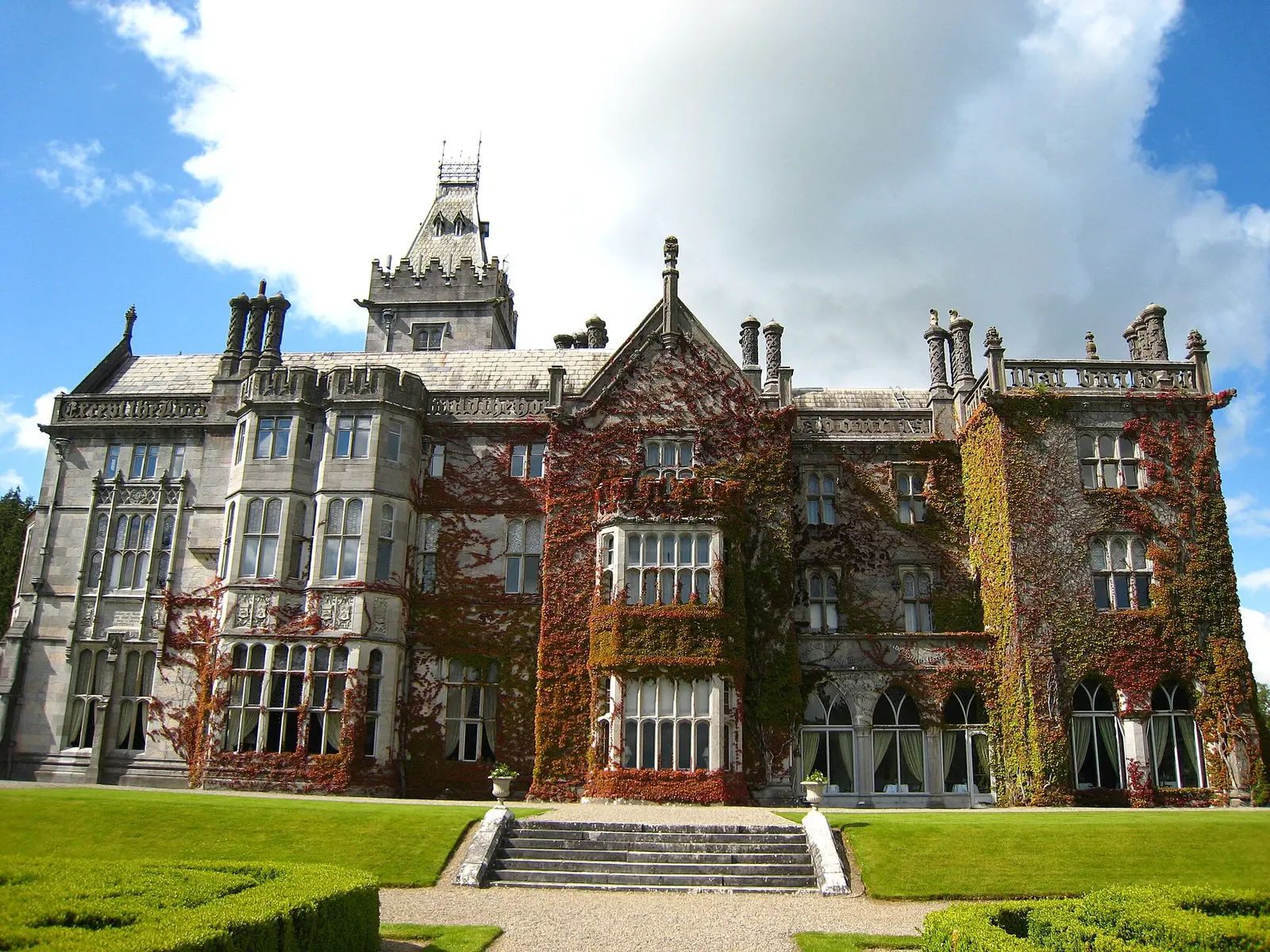 Ivy-covered neo-Gothic Adare Manor house seen across its lawn under a blue sky