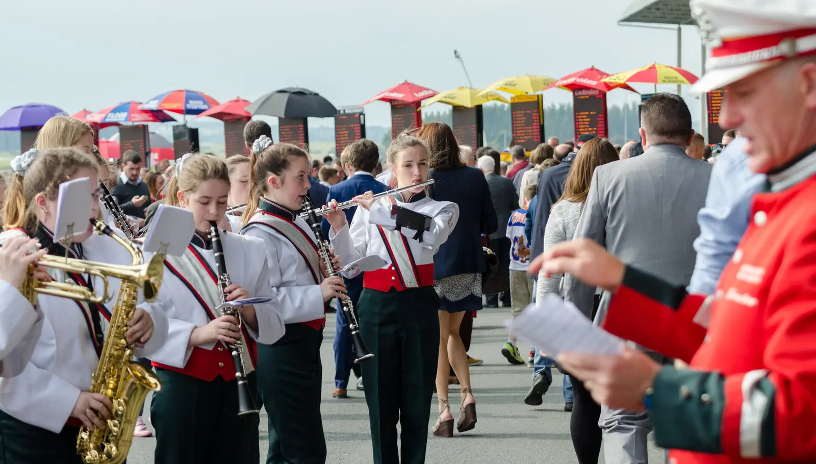 A school band in red and white uniforms plays among racegoers at the Curragh during Irish Champions Weekend