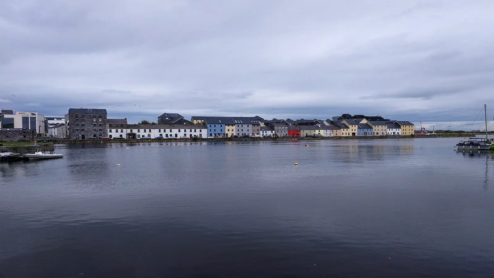 Colourful houses of the Long Walk across the water in Galway under a cloudy sky