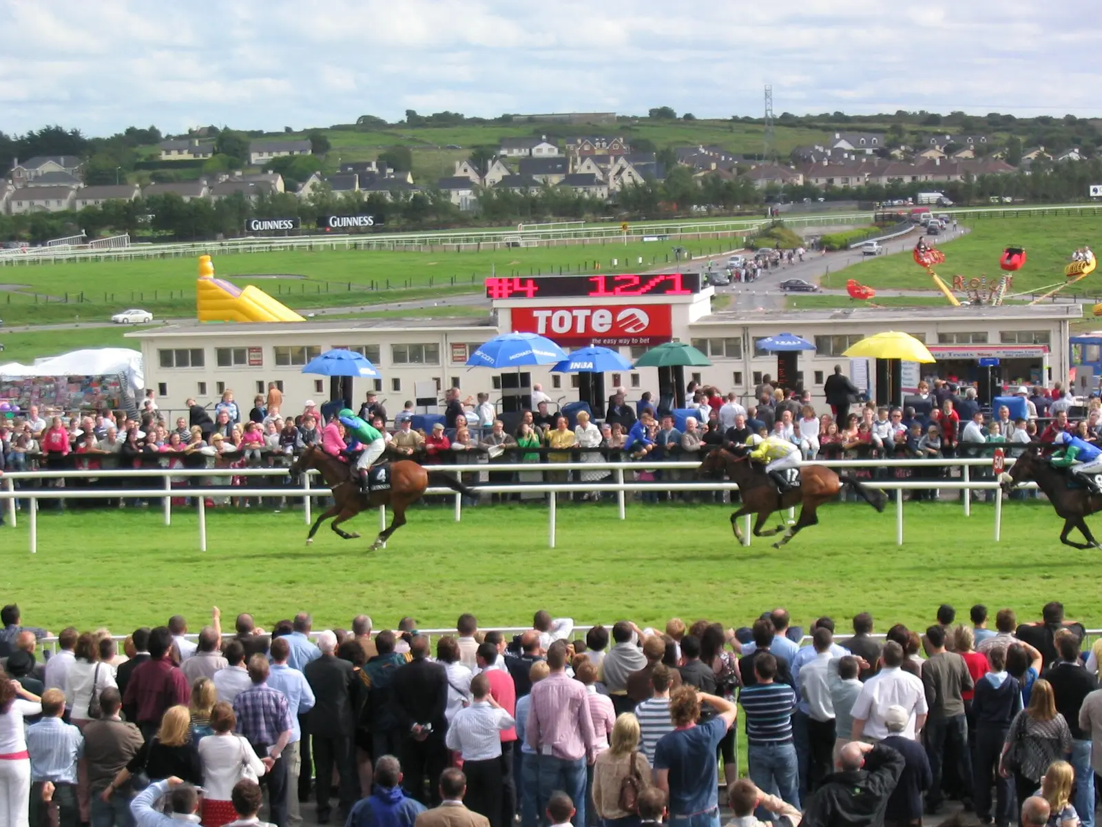 Horses racing past the crowd at Galway Racecourse with the grandstand behind