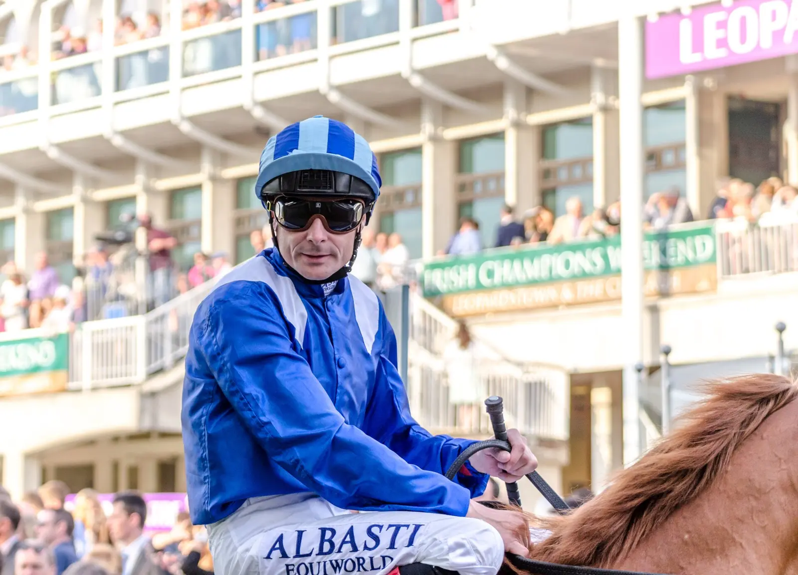 Jockey in blue silks in front of the Leopardstown grandstand during Irish Champions Weekend 2014
